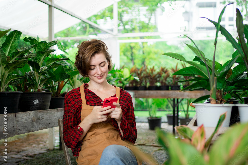 A woman is sitting on a chair and looking at her phone. She is smiling and seems to be enjoying herself. The scene is set outdoors, with a potted plant nearby. Scene is cheerful and relaxed A woman is sitting on a chair and looking at her phone. She is smiling and seems to be enjoying herself. The scene is set outdoors, with a potted plant nearby. Scene is cheerful and relaxed