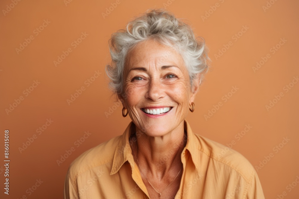 Portrait of a jovial woman in her 60s smiling at the camera isolated in pastel brown background Portrait of a jovial woman in her 60s smiling at the camera isolated in pastel brown background
