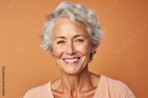 Portrait of a jovial woman in her 60s smiling at the camera isolated on pastel brown background