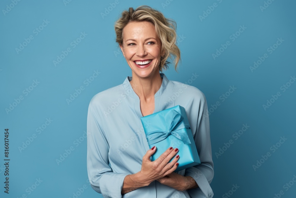 Portrait of a grinning woman in her 40s holding a gift on soft blue background Portrait of a grinning woman in her 40s holding a gift on soft blue background