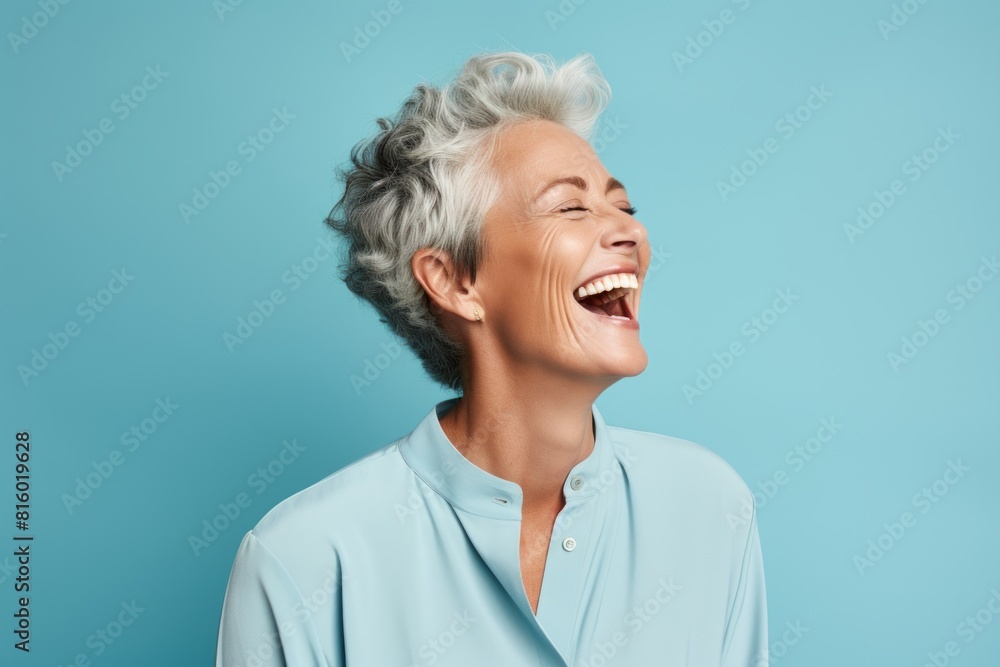 Portrait of a tender woman in her 60s laughing on soft blue background Portrait of a tender woman in her 60s laughing on soft blue background