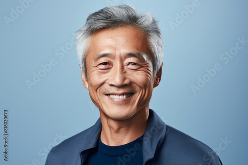 Portrait of a cheerful asian man in his 60s smiling at the camera in front of soft blue background