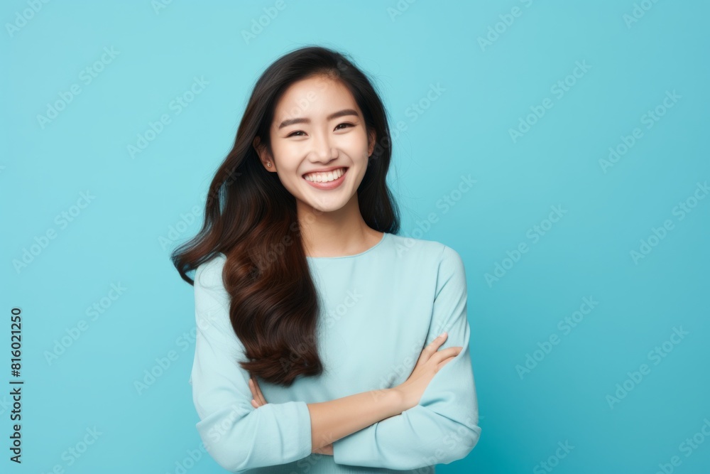 Obraz premium Portrait of a joyful asian woman in her 20s with arms crossed isolated in soft blue background