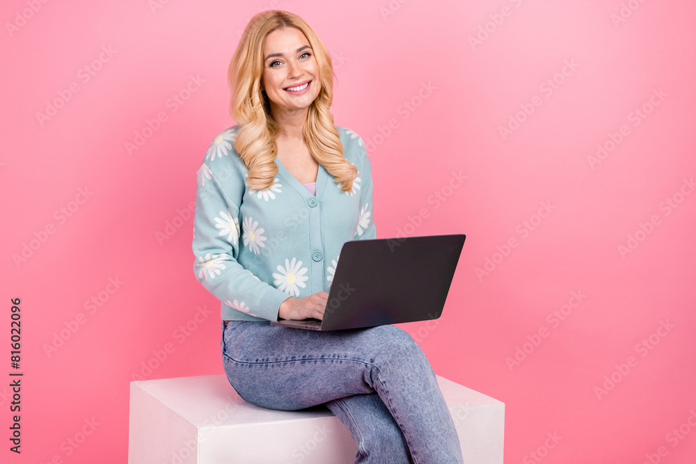 Photo portrait of lovely young woman sit white cube netbook dressed stylish flower print garment isolated on pink color background Photo portrait of lovely young woman sit white cube netbook dressed stylish flower print garment isolated on pink color background