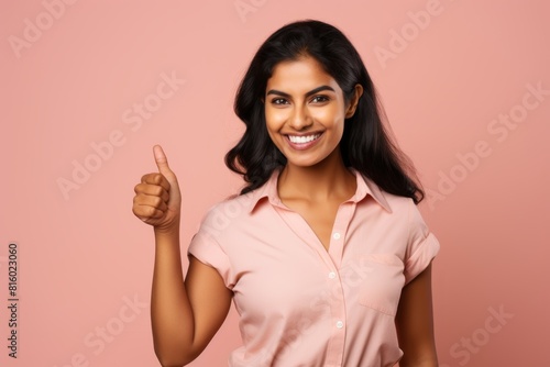 Portrait of a joyful indian woman in her 30s showing a thumb up isolated on soft pink background