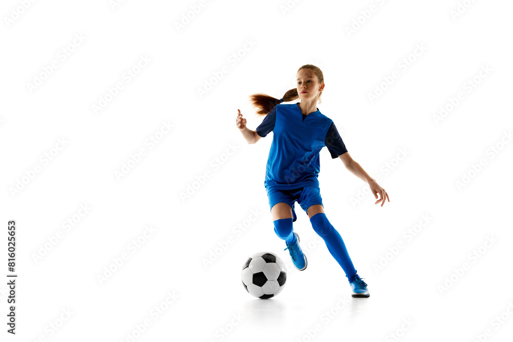 Fototapeta premium Concentrated teen girl in blue sportswear in motion, playing football, dribbling ball isolated on white studio background. Concept of sport, active and healthy lifestyle, childhood, school, hobby