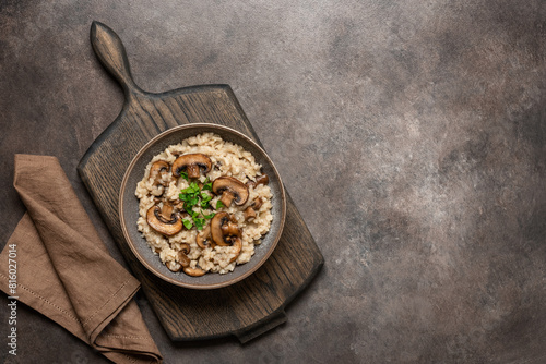 Risotto with brown champignon mushrooms in a bowl on a wooden board, dark rustic background. Top view, flat lay, copy space.