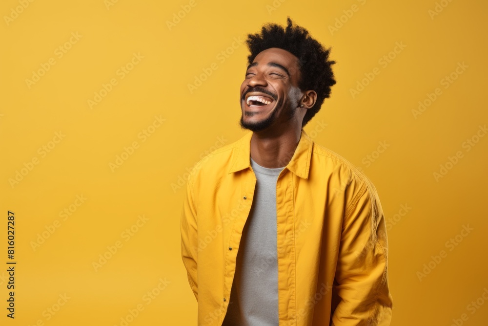 Fototapeta premium Portrait of a glad afro-american man in his 20s laughing while standing against soft yellow background
