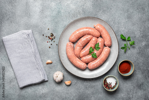 Raw sausages in a plate on a gray concrete background. Top view, flat lay.