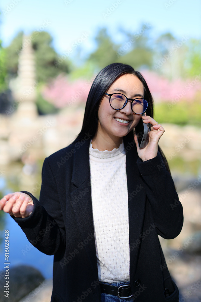 A positive Japanese businesswoman talks on her cellphone in the city, radiating confidence and professionalism. A positive Japanese businesswoman talks on her cellphone in the city, radiating confidence and professionalism.