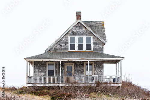 A charming coastal cottage with weathered shingles  a wraparound porch  and panoramic views of the ocean  exuding seaside charm against a solid white background.