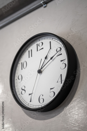 A classic round clock with numbers which is installed on white plain wall. Interior decoration object photo. Close-up and selective focus at some part of the clock.