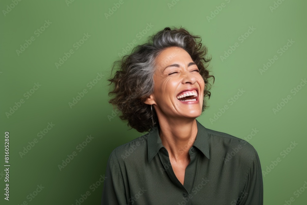 Portrait of a happy woman in her 50s laughing isolated in soft green background Portrait of a happy woman in her 50s laughing isolated in soft green background