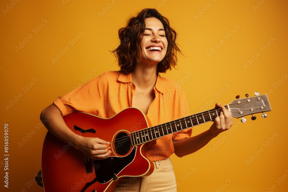 Portrait of a smiling woman in her 30s playing the guitar isolated on soft orange background Portrait of a smiling woman in her 30s playing the guitar isolated on soft orange background