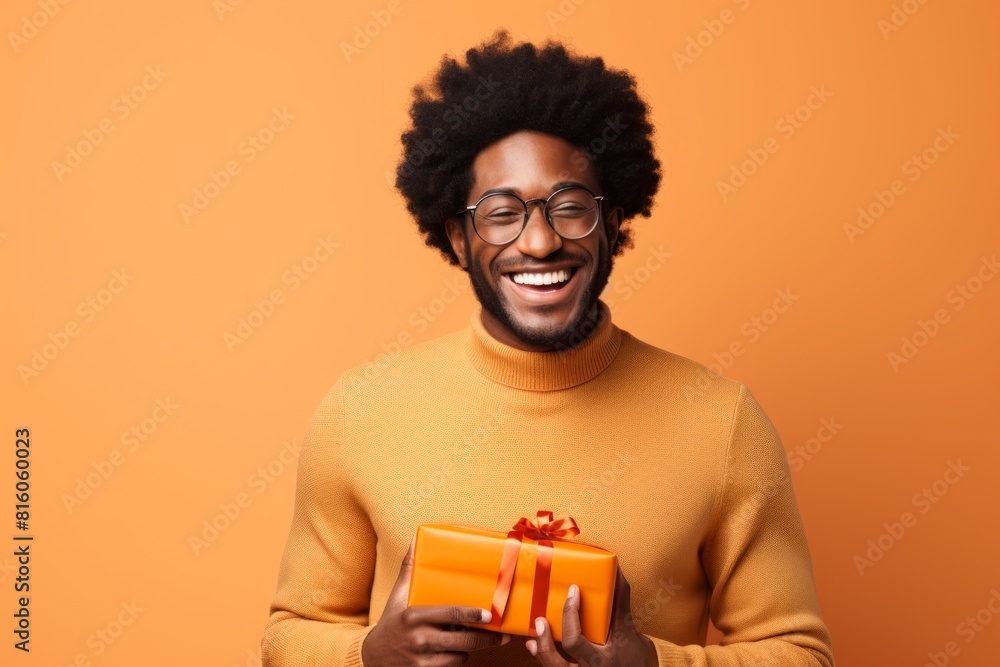 Portrait of a satisfied afro-american man in his 30s holding a gift while standing against soft orange background Portrait of a satisfied afro-american man in his 30s holding a gift while standing against soft orange background