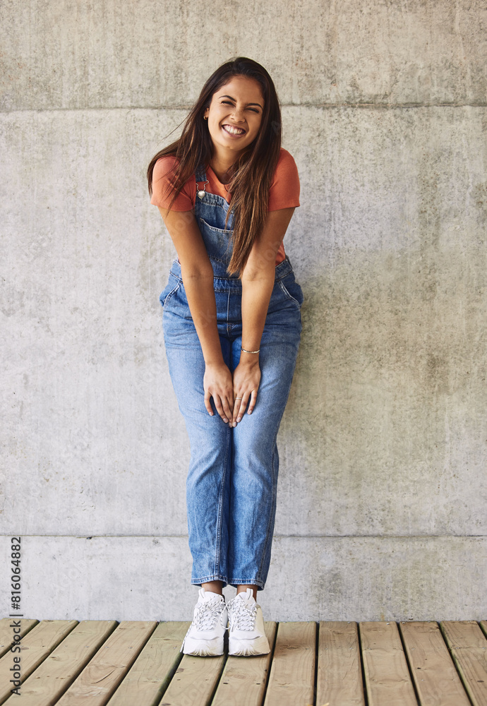 Fashion, smile and portrait of woman by wall with casual, trendy and dungaree outfit with sneakers. Happy, stylish and full body of female person with denim, trendy and funky clothes for confidence.