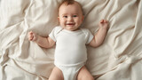 Sorridente bebezinho deitado na cama com roupa de cama bege. Criança vestindo macacão de bebê branco sólido em branco. Modelo de bodysuit recém-nascido neutro de gênero em branco simulado.