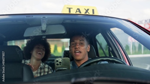 Happy African American taxi driver talking with lady sitting on the backseat. Yellow taxi car roof sign. People, job, service concept.