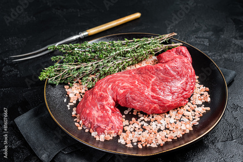 Raw Machete beef meat steak or hanging tender cut on plate with sea salt and thyme. Black background. Top view photo