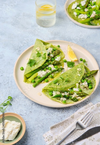 Green pancakes with spinach and nettles, stuffed with asparagus, green peas and ricotta on a ceramic plate on a gray concrete background. Seasonal products, recipes. Asparagus recipes.