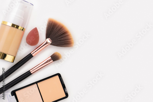Sponge and a bottle of beige cosmetic foundation, brushes for make-up and face powder on white table background, close-up. Makeup artist and woman accessories for perfect face skin, beauty. Copyspace.