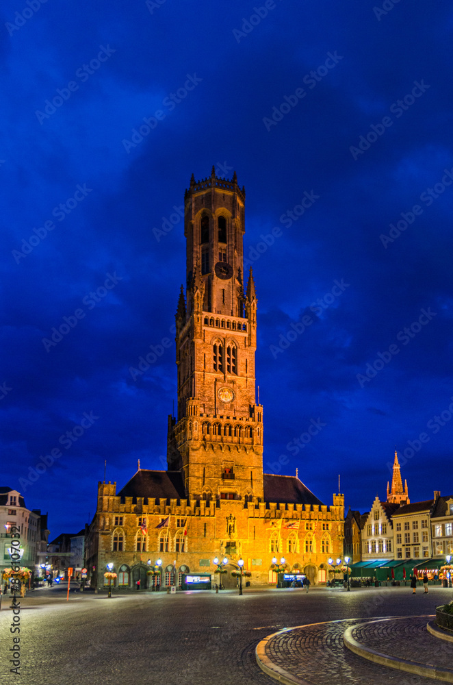 Naklejka premium Belfry of Bruges Belfort van Brugge medieval bell tower on Markt Market square in Brugge old town Steenstraat quarter, Bruges city historical centre, evening view, West Flanders province, Belgium