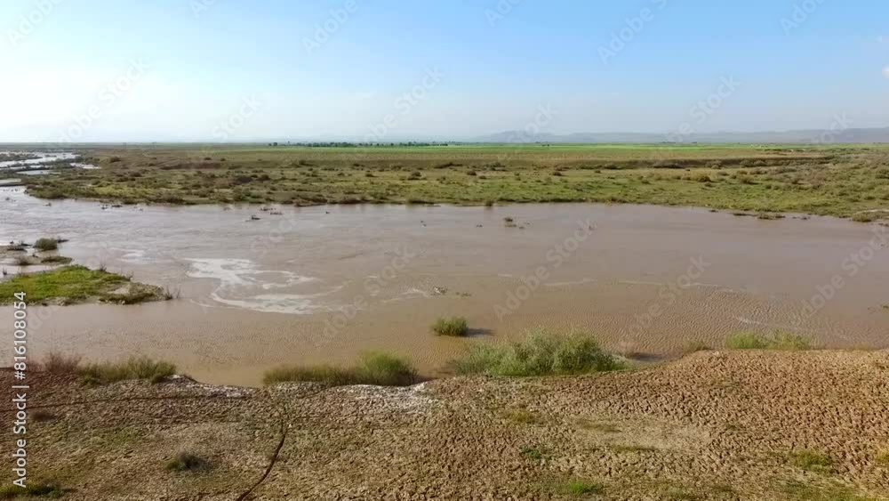 Aerial view of a desert river flowing with water, transforming the landscape into a green and lush oasis under a sunny, clear sky. Aerial view of a desert river flowing with water, transforming the landscape into a green and lush oasis under a sunny, clear sky.