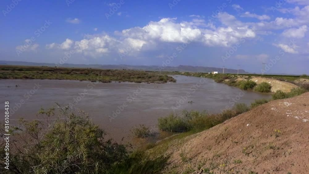 Long shot of a wide river flowing through a green landscape, under a picturesque sky with large fluffy clouds in distance. Long shot of a wide river flowing through a green landscape, under a picturesque sky with large fluffy clouds in distance.