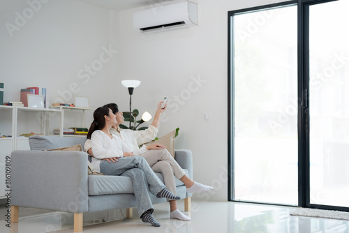 Couple relaxing on couch adjusting air conditioner with remote control