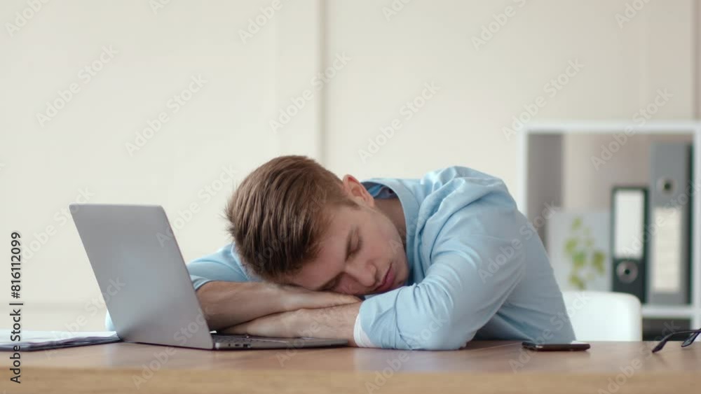 Tired young man sleeping on laptop at workplace table, working from home Tired young man sleeping on laptop at workplace table, working from home