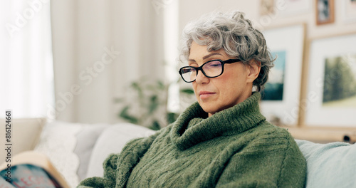 Woman reading funny book in living room for story, novel and knowledge in retirement. Happy senior female person relax with books in lounge for break, literature and hobby to enjoy on sofa at home