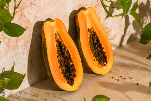 Halved papaya with seeds, hard shadows and a plant