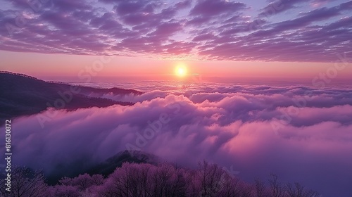   The sun is setting over the clouds in the sky above a foggy valley between mountains