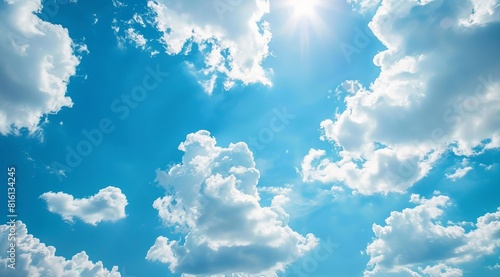 A bright and refreshing wallpaper of a clear blue sky dotted with fluffy white clouds and a gleaming sun peeking through, capturing the beauty of nature