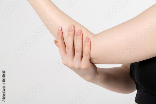 Close-up view of caucasian woman rubbing her elbow using hand against grey background. Soft focus. Healthcare, cosmetics and self massage theme.	