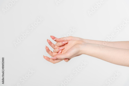 Close-up side view of elegant female hands holding each other against grey background. Soft focus. Femininity and sensuality. Beauty and body care. Relationship bonds. Self expression theme.