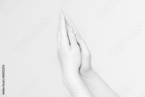 Close-up side view of elegant female hands holding each other in praying gesture against grey background. Black and white photography. Soft focus. Spirituality and religious occupation theme.