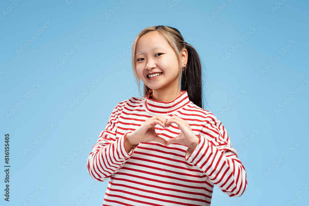 Happy cute Asian girl showing heart shape by hands looking at camera, isolated Happy cute Asian girl showing heart shape by hands looking at camera, isolated