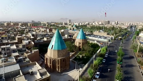Aerial perspective of the historic green domes set amidst the dynamic urban life of Qom, with one dome uniquely connected to a bustling highway by an asphalt road. photo
