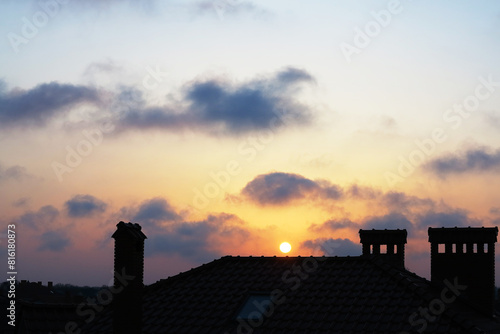 Chimneys, tiled roof of a house and beautiful clouds in the haze at sunset