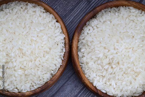 Raw white rice on wooden background. Long uncooked rice in wooden plate. Natural organic food. Traditional Asian cereal culture.