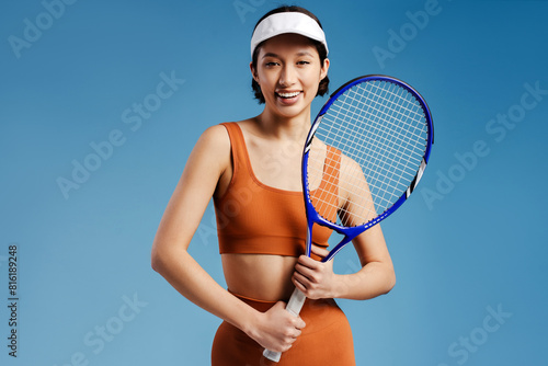 Young asian woman in sportswear holding racket and posing over isolated blue background © Maria Vitkovska