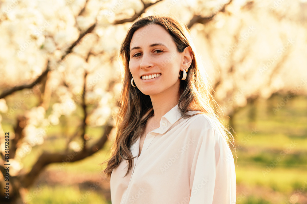 Young cheerful woman standing in blossom-filled orchard on a sunny day. Young cheerful woman standing in blossom-filled orchard on a sunny day.