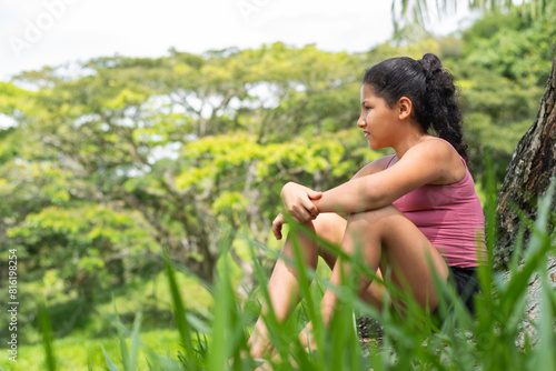 latina brunette girl sitting next to a tree looking towards the horizon very pensive photo