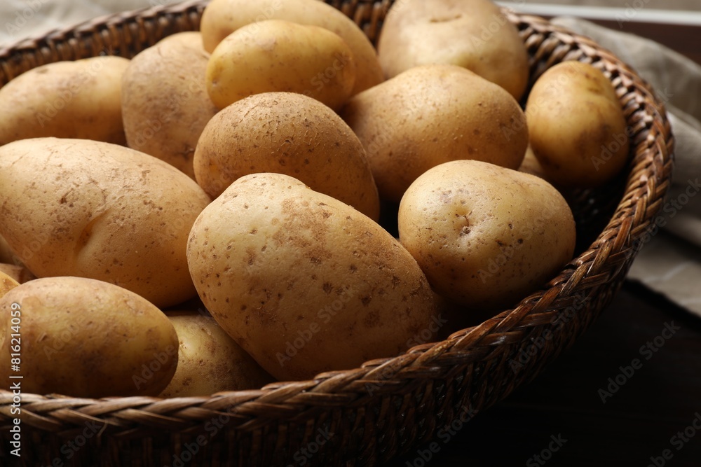 Raw fresh potatoes in wicker basket on wooden table, closeup Raw fresh potatoes in wicker basket on wooden table, closeup