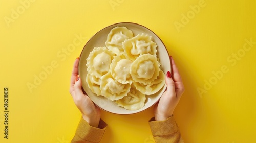 Flat lay of female hands holding a plate of ravioli or dumplings with a top view on a yellow background