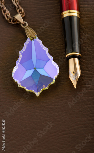 Fountain pen and crystal positioned on brown leather surface, selective focus