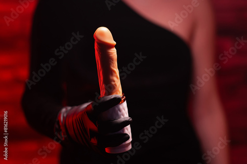 Automatic telescopic silicone dildo for masturbation in a female hand in black gloves and a black dress on a red background. Products for sex shop, adult gifts for couples