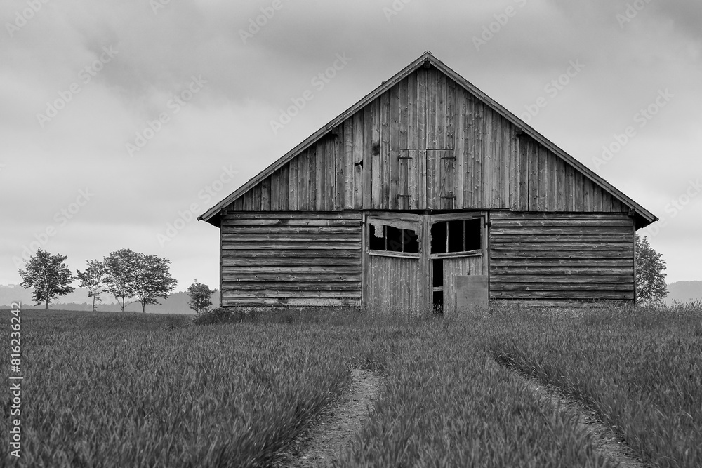 Old wooden barn in black and white surrounded by fields with tire tracks through the field towards the barn. Rustic charm of rural landscape. Old wooden barn in black and white surrounded by fields with tire tracks through the field towards the barn. Rustic charm of rural landscape.