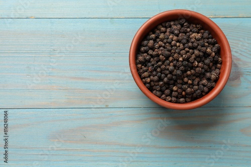 Aromatic spice. Black pepper in bowl on light blue wooden table, top view. Space for text